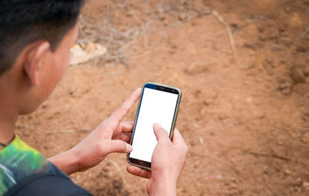 Close up of a man with cell phone in hand, close up of hands with cell phone with white screen, young guy with cell phone in hand with copy spaceの写真素材