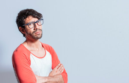 Young latin man in glasses with crossed arms looking in profile at the camera. Nicaraguan man with crossed arms looking at the camera isolated, Portrait of young man with crossed arms isolatedの写真素材