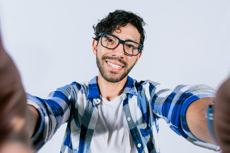Handsome man taking a selfie looking at the camera on isolated background. Teenage guy taking a self portrait isolated. Guy with beard and glasses taking a self portrait isolatedの写真素材