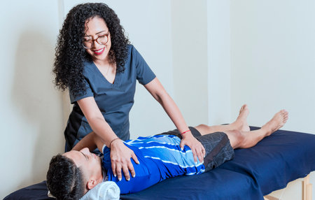 Physiotherapist with patient on back treatment, back rehabilitation physiotherapy, smiling female physiotherapist practicing back rehabilitation to patientの写真素材