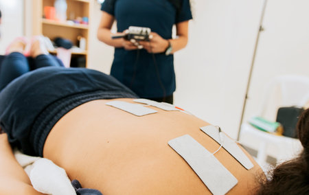 Physiotherapist electrostimulating a patient, Electrode treatment to patient lying down, Professional physiotherapist electrostimulating a lying patient. Lower back therapy with electrode padsの写真素材