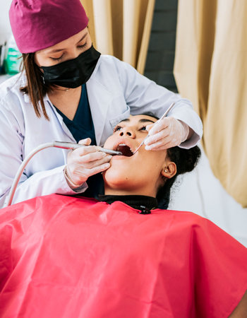 Professional dentist cleaning a female patient's mouth, Female dentist cleaning and examining a...