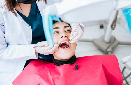Top view of dentist doing cleaning to female patient lying down. Dentist doctor examining mouth to patient lying on chair, Female dentist examining mouth to patient lying downの写真素材
