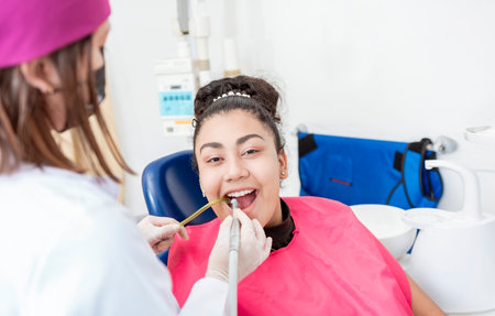 Stomatologist woman with drill cleaning patient girl mouth. Stomatologist drilling and cleaning a patient teeth, Woman stomatologist drilling patient teeth looking at the cameraの写真素材