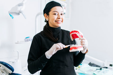 Smiling female dentist showing a denture, Dentist explaining tooth brushing, female dentist showing...