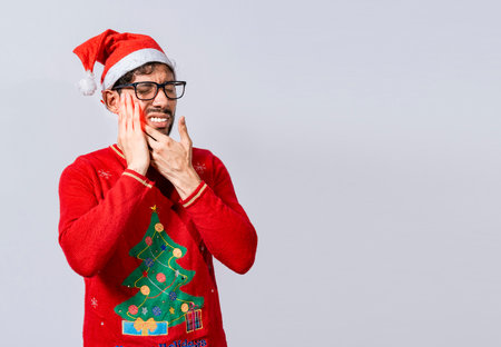 Man in christmas sweater with toothache, Young man in christmas hat with toothache isolated, Man in christmas hat in pain touching his tooth. Christmas toothache conceptの写真素材
