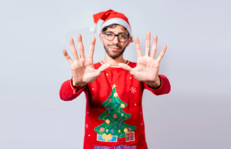 Man in christmas hat counting number ten with fingers. Christmas young man counting number ten with hands. Concept of man in christmas costume counting number ten isolatedの写真素材