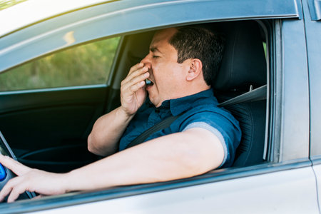 Tired driver yawning, concept of man yawning while driving. A sleepy driver at the wheel, a tired person while drivingの写真素材