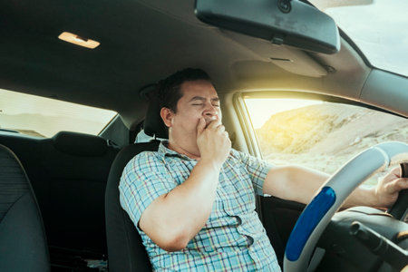 View of a sleepy driver in his car. Tired driver yawning in the car, concept of man yawning while driving. A sleepy driver at the wheel, a tired person while drivingの写真素材