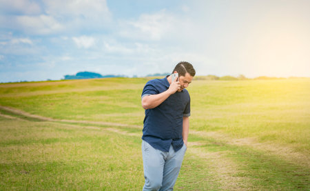 Person with his cell phone in the field talking on the phone, Man calling on the phone in the field, man on a road talking on the phone, young person talking on the phone in a fieldの写真素材