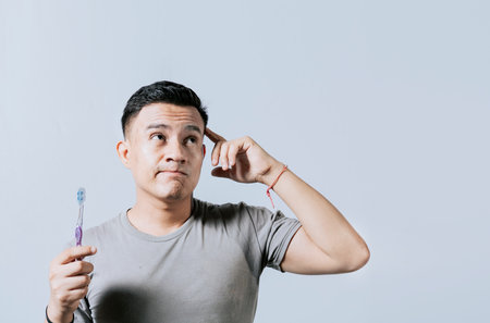 Man holding toothbrush with thoughtful expression isolated. Person holding toothbrush looking up,...