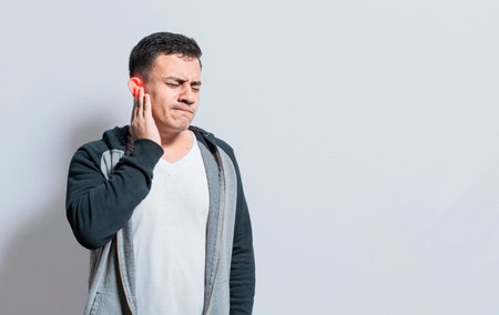 Person with ear pain, on isolated background, Suffering man massaging his ear isolated, A person with otitis and tinnitusの写真素材