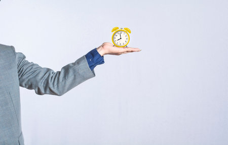 A hand holding a table clock on isolated background, close up of a hand holding an alarm clock, businessman hand holding clock isolatedの写真素材