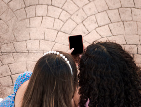 friend showing her cell phone screen, two girls pointing at her cell phone, Girl showing her smartphone to her friendの写真素材