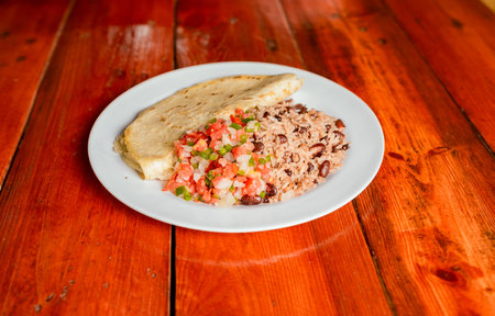 Gallopinto dish with quesillo and pico de gallo on wooden table. Traditional Gallo Pinto Meal with Pico de Gallo and quesillo servedの写真素材