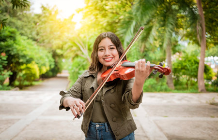 Young woman playing the violin outdoors. Portrait of a girl playing the violin outdoors, Close up of a girl with her violin playing a melody outdoors, Concept of smiling female violinistの写真素材