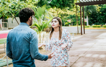 Unhappy couple standing arguing in a park. Disgusted teenage couple arguing in a park, Man and woman...