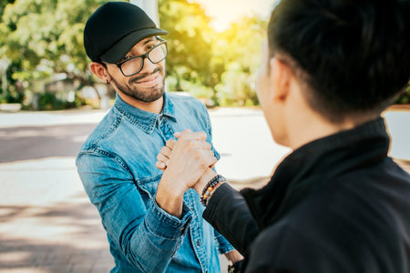 Concept of two friends greeting each other and shaking hands on the street. Two teenage friends shaking hands at each other outdoors. Two people shaking hands on the streetの写真素材