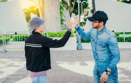 Side view of people greeting each other and shaking hands on the street. Two teenage friends shaking hands outdoors. Concept of two friends greeting each other with a handshake on the streetの写真素材