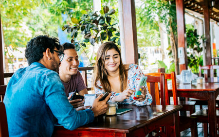 Young friends in a coffee shop with their cell phones having a good time. Three people in a coffee...