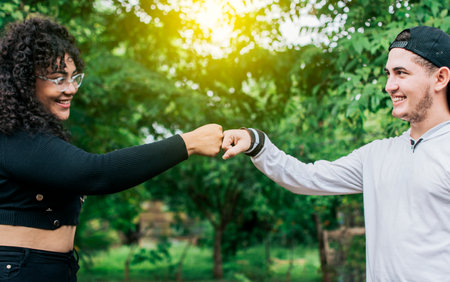 Two young teenage girls bumping their fists outdoors, Two smiling friends bumping their fists,...