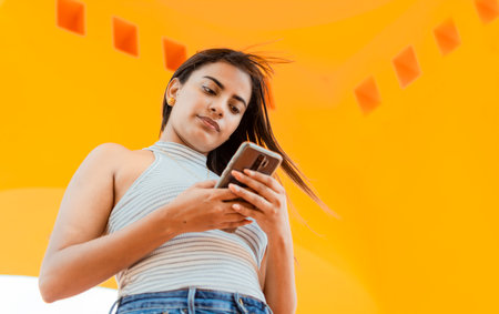 Portrait of attractive latin girl messaging on cell phone. Low angle of a beautiful Latin girl using the smart phone. Low angle of a young latin woman texting on cell phoneの写真素材