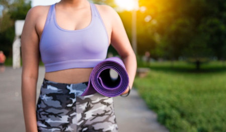Unrecognizable woman holding a mat in the park. Athlete woman's hands carrying the mat after exercising. Fitness woman concept carrying yoga mat with copy spaceの写真素材