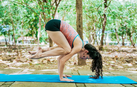 Young woman doing yoga crow pose outdoors. Girl doing yoga bakasana or crow pose in nature.