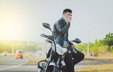 Biker sitting on motorcycle calling on the phone on the roadside. Handsome biker calling on the phone in the street. Concept of motorcyclist using the phoneの写真素材