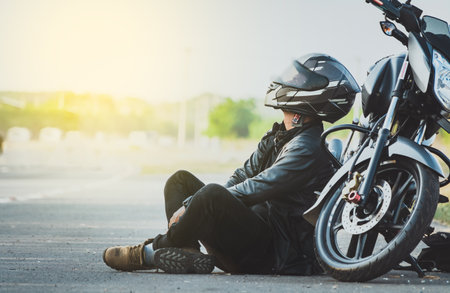 Biker sitting next to his motorcycle on the road. Male motorcyclist sitting and leaning on his motorcycle on the asphaltの写真素材