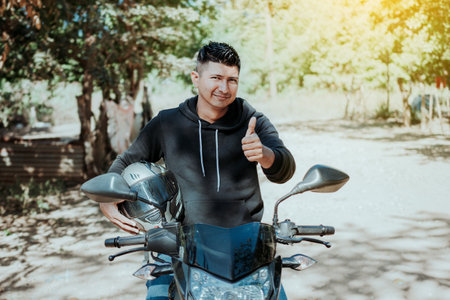 Biker on his motorbike holding safety helmet with thumb up. Concept of Smiling motorcycle cyclist...