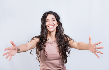 Happy young latin woman welcoming with open arms isolated. Hospitable girl opening arms to the camera. Smiling girl asking for a hugの写真素材