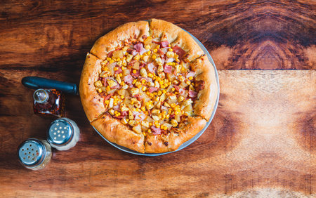 Top view of ham and corn pizza on wooden table. Ham pizza with corn on wooden backgroundの写真素材