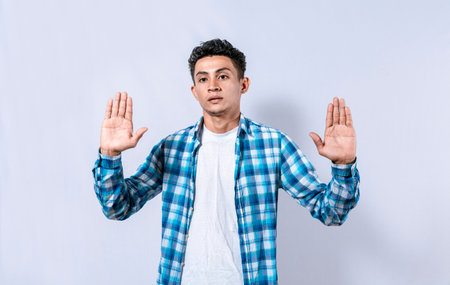 Scared and horrified man with raised palms, Man with a frightened face with his hands raised in front. Portrait of scared person with raised hands, Scared guy with raised hands in frontの写真素材