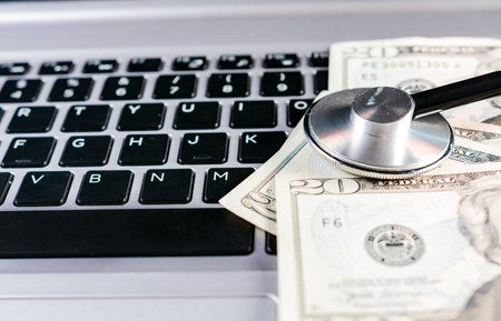 Stethoscope on dollar bills on top of laptop keyboard. Stethoscope on top of money on laptop keyboardの写真素材
