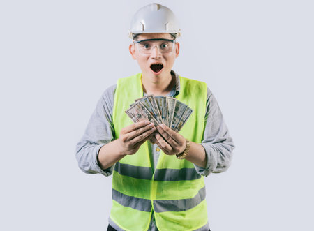 Surprised engineer in helmet holding money isolated. Amazed male engineer holding banknotes on isolated backgroundの写真素材