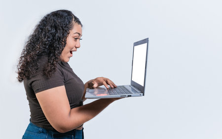 Surprised girl looking at a promotion on laptop screen isolated. Amazed latin woman using laptop isolated. Latin people looking offer promo on laptop isolated.の写真素材