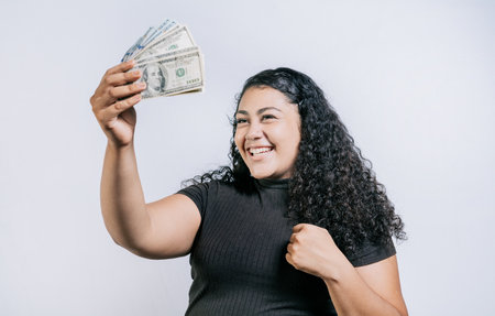 Excited latin girl holding dollar cash isolated. Victorious young woman holding money celebrating isolatedの写真素材