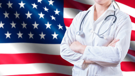Female doctor with stethoscope on American flag. Unrecognizable female doctor with arms crossed on American flag, Health and care with the flag of United Stateの写真素材