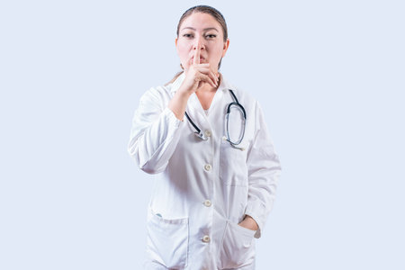 Female doctor making silence gesture isolated. Beautiful female doctor silencing and looking at the cameraの写真素材