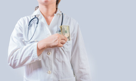 Unrecognizable doctor putting bribe money in pocket isolated. Dishonest female doctor putting money in pocket. Medical bribery conceptの写真素材