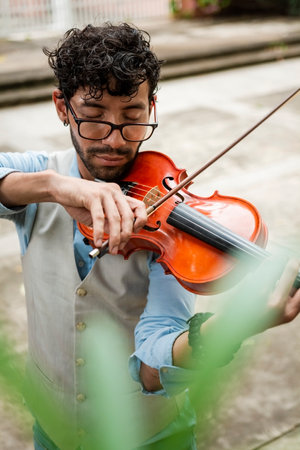 Handsome man in vest playing violin outdoors. Close up of violinist man playing a melody outdoors. Violinist artist playing a melody outdoors.の写真素材