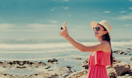 Young woman on vacation taking photos on the beach, Smiling girl in hat taking photos on the beach....