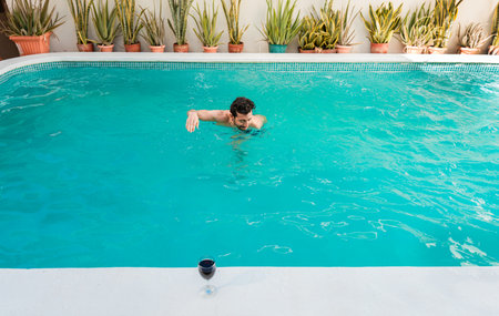 Handsome man on vacation swimming in a hotel pool, Man on vacation swimming in a blue swimming pool. Young man swimming in a tropical hotel poolの写真素材