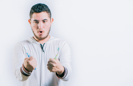 Surprised handsome guy holding toothbrushes isolated. Amazed teen guy holding two toothbrush isolatedの写真素材