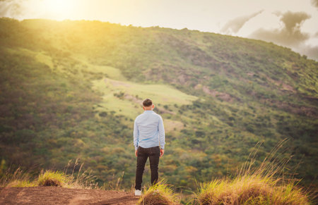 Back view of a man on a hill at sunset. Rear view of a man on top of a hill looking at the horizonの写真素材