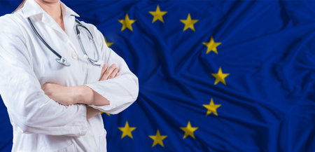 Doctor with crossed arms on European Union flag. European Union health and care concept. Female doctor on European Union flagの写真素材