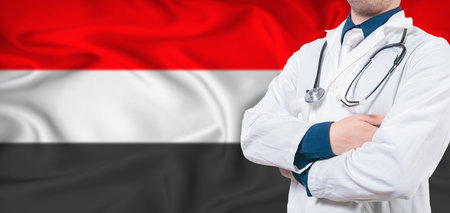 Yemen healthcare concept. Male doctor on Yemen flag. Doctor with crossed arms on Yemen flagの写真素材