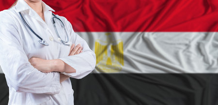 Doctor with crossed arms on Egypt flag. Egypt health and care concept. Female doctor on Egypt flagの写真素材