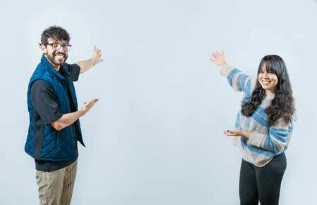 Happy couple showing something and smiling at the camera, isolated. Young couple presenting something smiling at cameraの写真素材